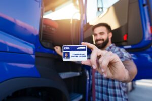 Portrait of a middle-aged bearded truck driver standing by his truck and showing his commercial driver's license (CDL). Focus on the CDL license. 